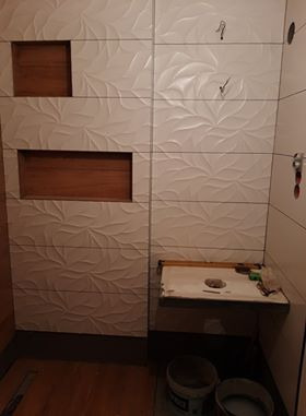 Białe, trójwymiarowe płytki ceramiczne z motywem liści na ścianie kabiny prysznicowej, z wnękami wyłożonymi drewnem, w trakcie montażu.