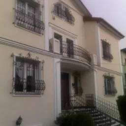 Dwupiętrowy dom z kremową elewacją, zdobionymi, czarnymi balustradami okiennymi i balkonem, widok z dołu na wejście z schodami.