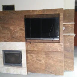 Obudowa kominka z marmurową okładziną, wnęka na telewizor z widocznymi kablami, półki z marmuru po prawej stronie, całość w surowym stanie, podłoga nie wykończona.