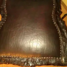 Czarne skórzane siedzisko krzesła z metalową ramą imitującą korę drzewa, zdobione nitami. Widok z góry, bliskie ujęcie na detal wykończenia.