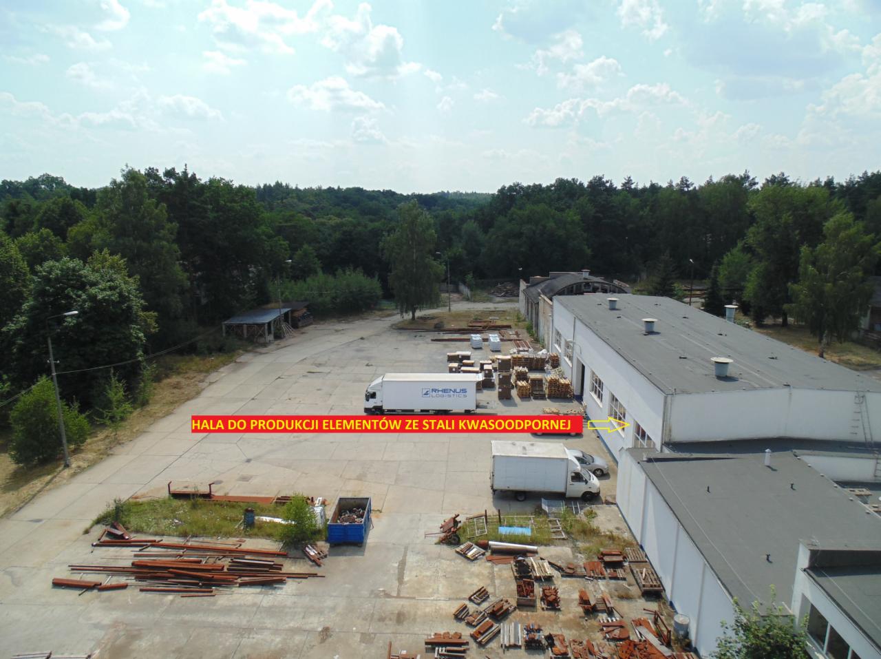 Widok z lotu ptaka na halę produkcyjną elementów ze stali kwasoodpornej, z zaparkowanymi ciężarówkami i składowanymi elementami na zewnątrz.
