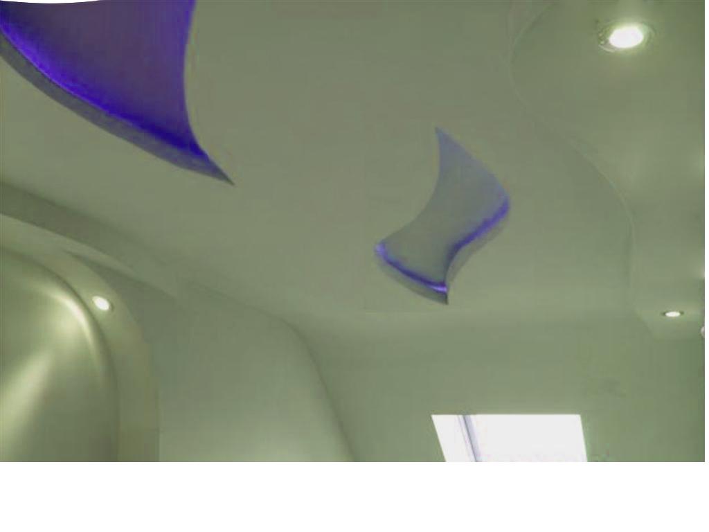 Sufit podwieszany z oryginalnym kształtem i niebieskim podświetleniem LED, widoczne punkty świetlne i fragment okna.