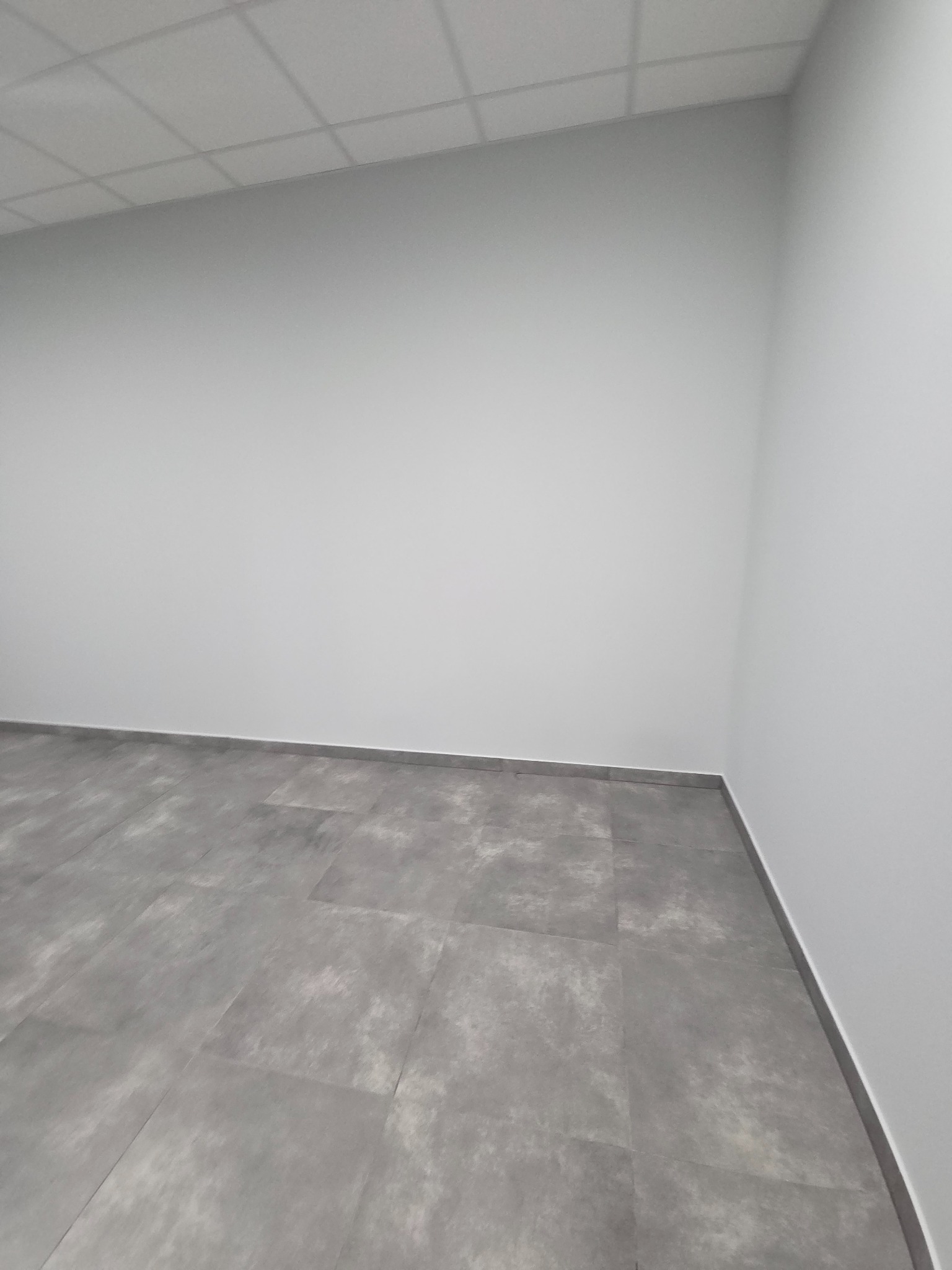 Szare płytki podłogowe w nowym, pustym pokoju z białymi ścianami i sufitem kasetonowym. Minimalistyczne wykończenie wnętrza, widok z góry.