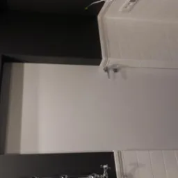 Wykończona ściana łazienki z czarną farbą, białą glazurą i heksagonalnymi płytkami. Widoczne baterie umywalkowe.