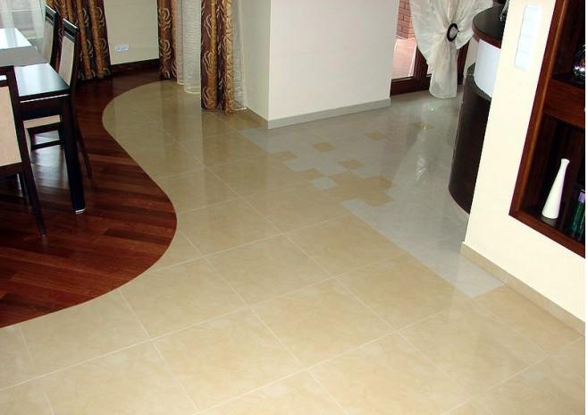 Beżowa podłoga z płytek ceramicznych przechodząca w parkiet ułożony w łuk, widoczne elementy instalacji wodno-kanalizacyjnej pod podłogą w postaci jasnych kwadratów