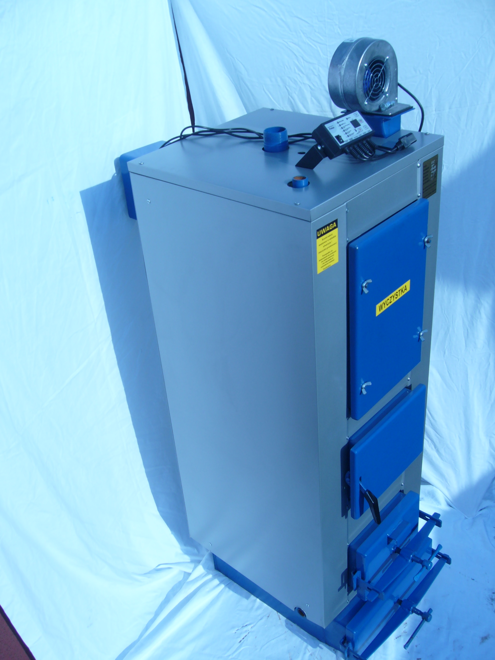 Nowy, szaro-niebieski kocioł na paliwo stałe z wentylatorem i panelem sterowania na górze, sfotografowany na białym tle.