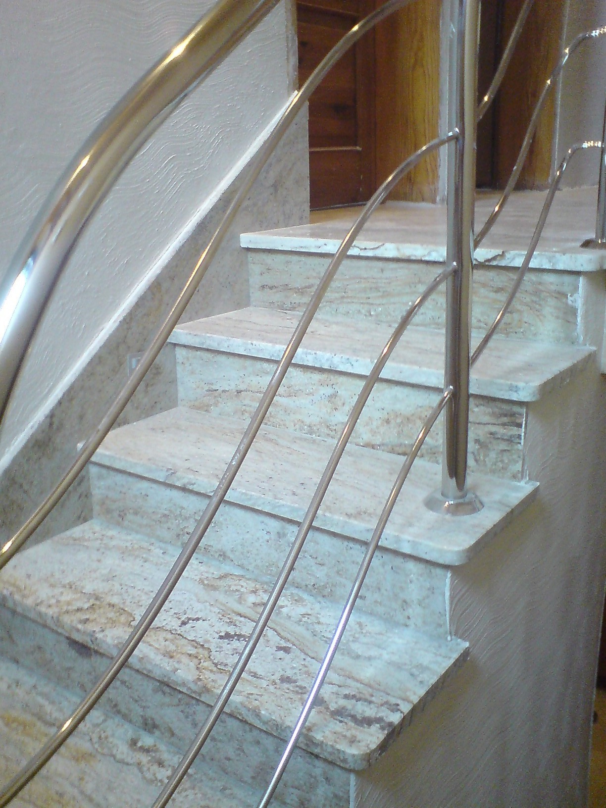 Schody wyłożone płytami imitującymi marmur, z nowoczesną, metalową balustradą o minimalistycznym designie.