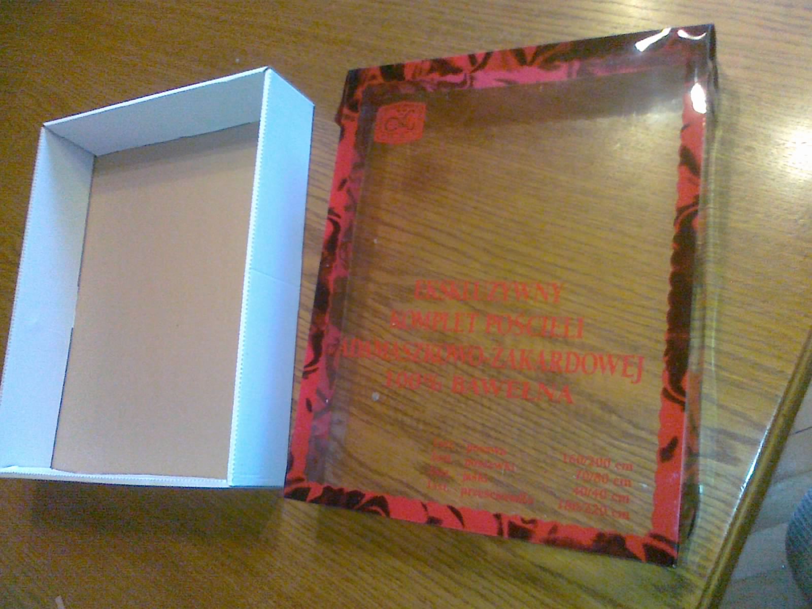 Pudełko kartonowe z wieczkiem z tworzywa sztucznego z nadrukiem, otwarte, widok z góry, na drewnianym blacie.