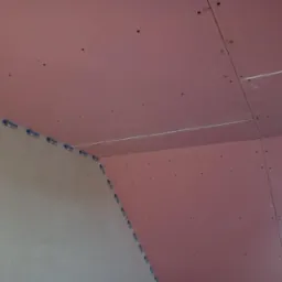 Montaż różowej płyty Rigips na skośnym poddaszu, widoczne łączenia i taśma wzmacniająca, przygotowanie do dalszych prac wykończeniowych.