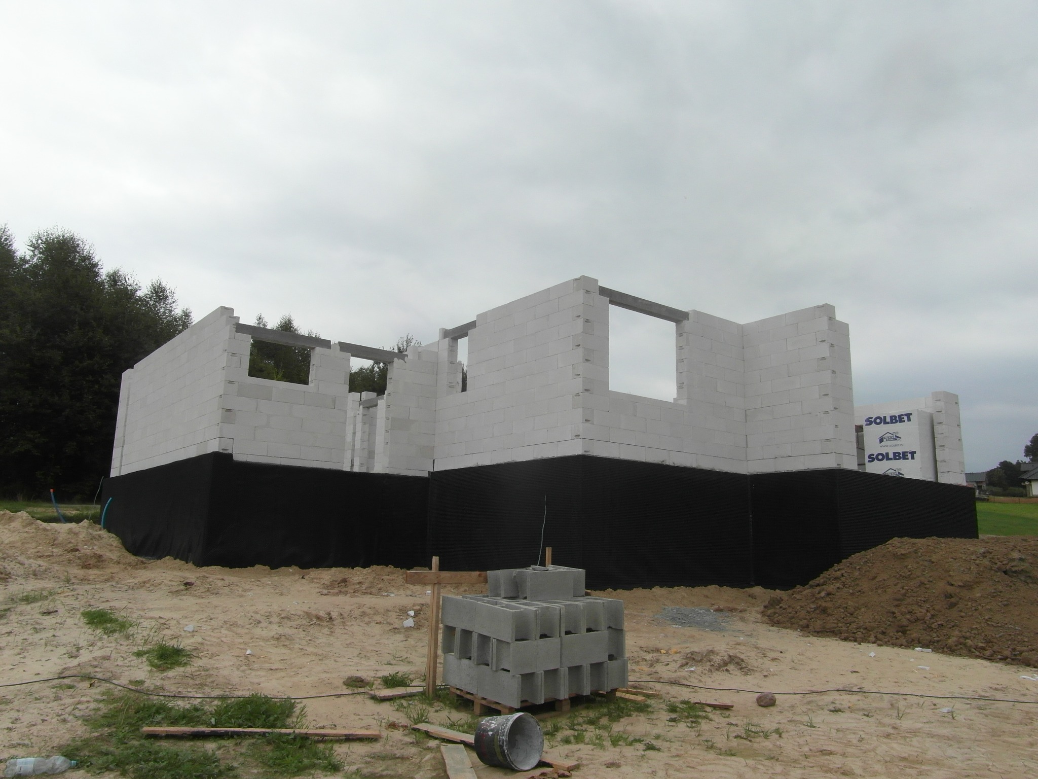 Wznoszenie ścian domu z betonu komórkowego w Raniżowie, widoczne fundamenty zabezpieczone czarną folią oraz paleta z bloczkami Solbet.