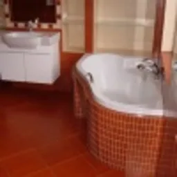 Jasna łazienka z wanną obłożoną mozaiką w odcieniach brązu, umywalką z szafką i terakotową podłogą. Widoczne elementy wykończenia z drewna w ciepłym odcieniu.