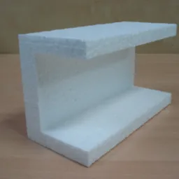 Kształtka styropianowa w kształcie litery C, leżąca na drewnianym blacie, widoczna struktura porowatego materiału.