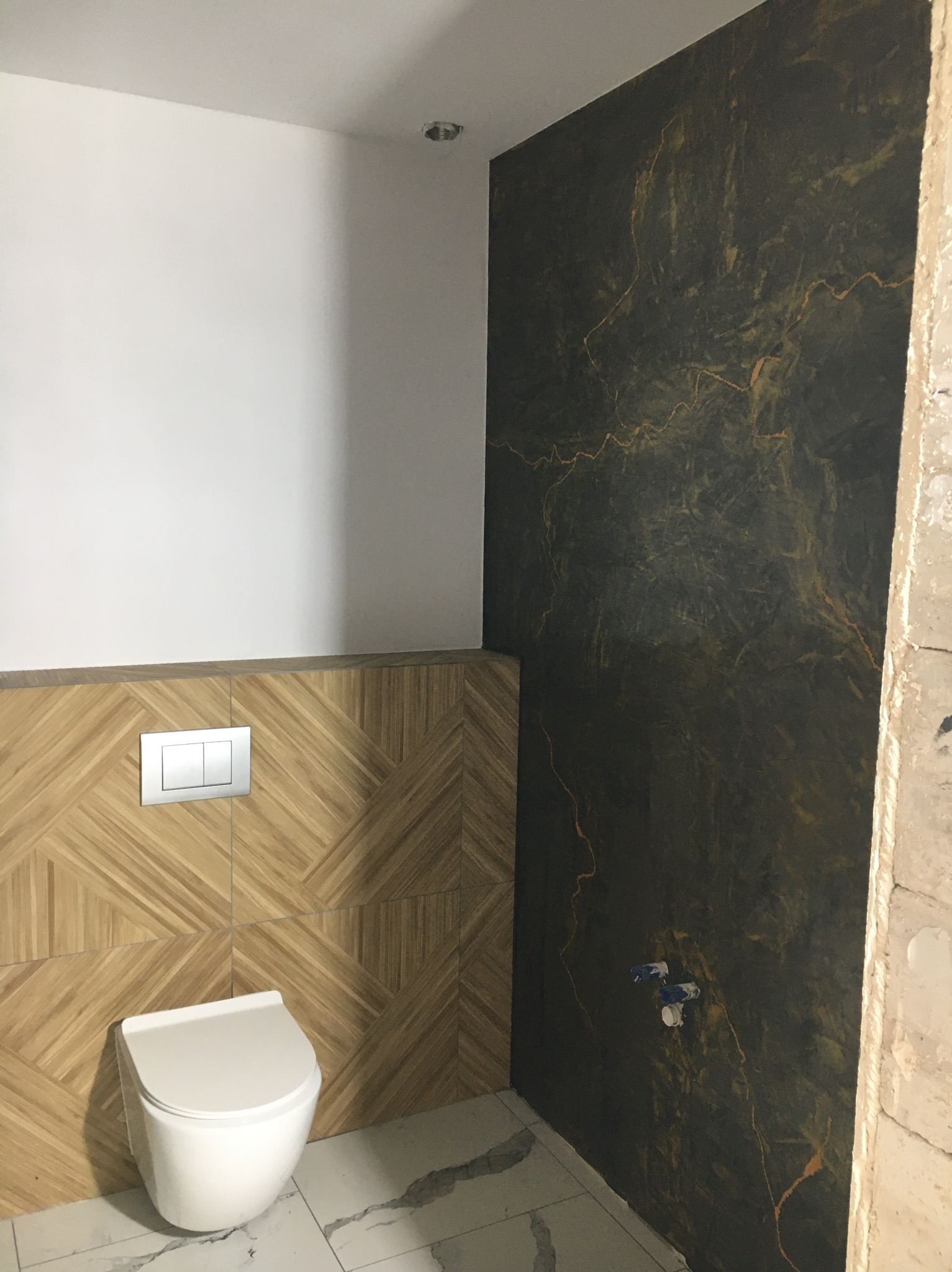 Wykończona łazienka: ściana z efektem marmuru, geometryczne panele drewnopodobne, biała ceramika i marmurowe płytki podłogowe. Nowoczesny design.