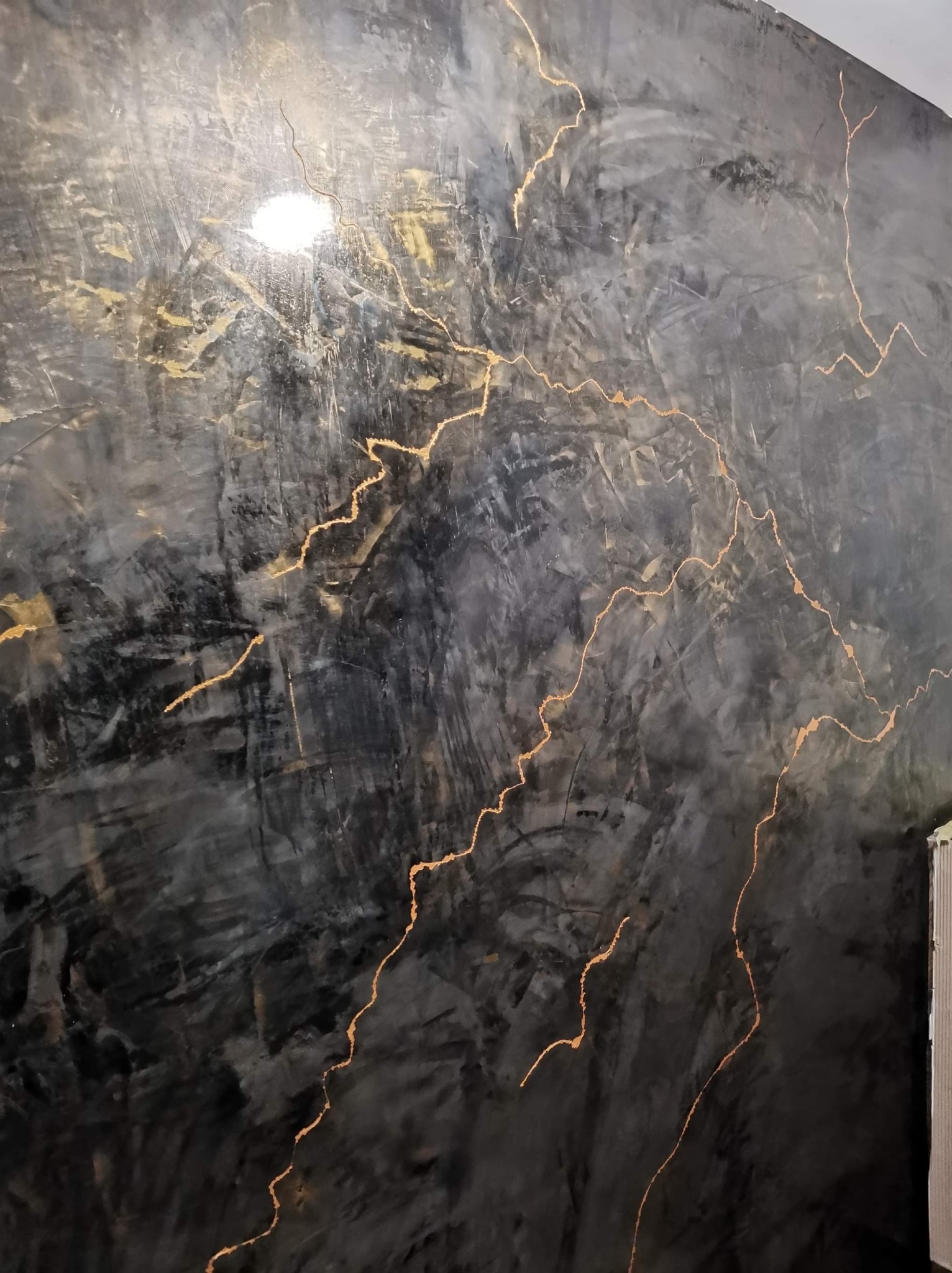 Czarna ściana z efektem betonu i złotymi żyłkami, dekoracyjne wykończenie wnętrza, oświetlenie punktowe podkreśla fakturę.