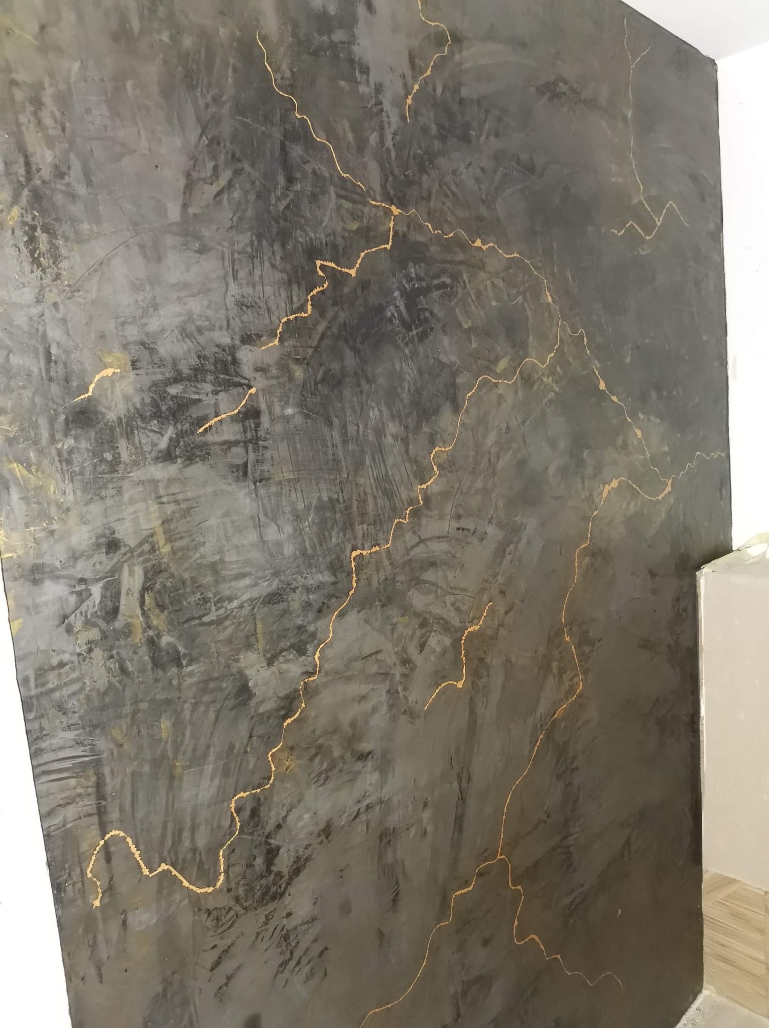 Dekoracyjna ściana w odcieniach szarości z nieregularnymi, złotymi żyłkami, imitująca beton. Wykończenie wnętrza z efektem wizualnym.