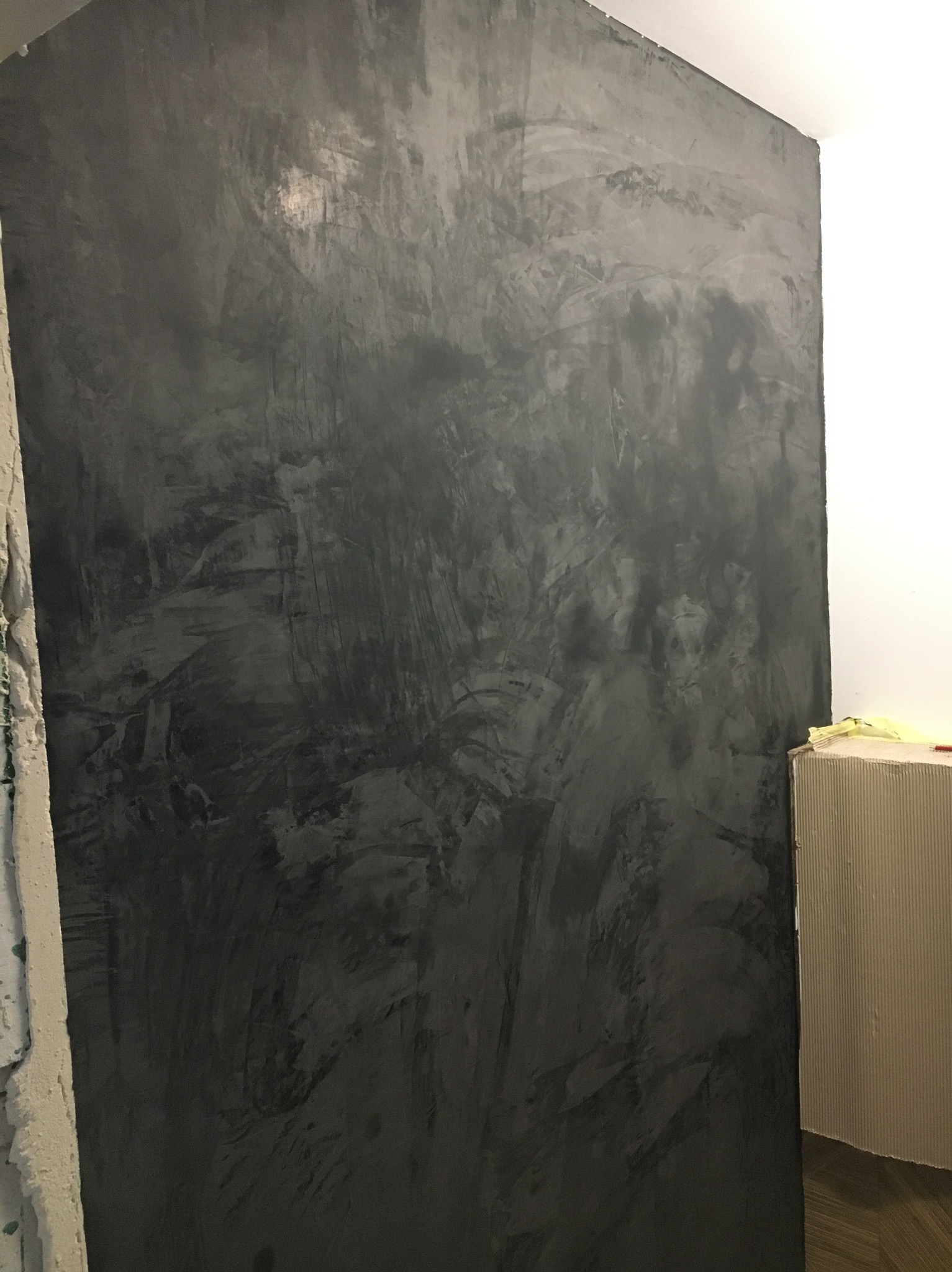 Ściana z efektem dekoracyjnym w odcieniach szarości, imitująca beton, z widocznymi śladami pędzla i nierównomiernym rozłożeniem koloru, wykończona w rogu pomieszczenia.