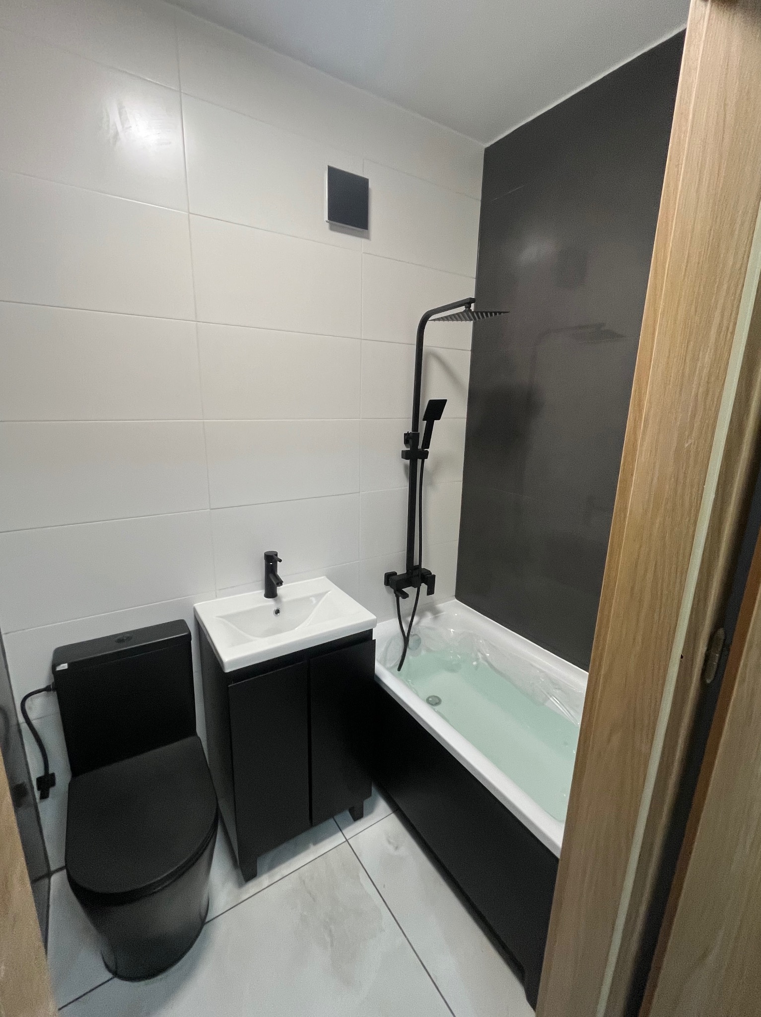 Nowoczesna łazienka po remoncie: białe płytki, czarna armatura i meble, wanna z deszczownicą. Minimalistyczny design z akcentem na kontrast kolorów.