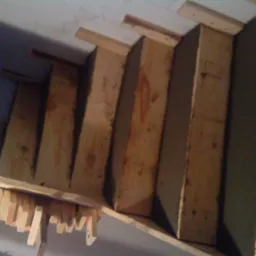 Surowe drewniane schody w trakcie budowy, widoczne elementy konstrukcyjne i deski, przymocowane do ściany.