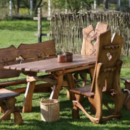 Rustykalny komplet mebli ogrodowych z litego drewna: stół, ławka i krzesła z wyciętymi sercami w oparciach, ustawione na trawniku w ogrodzie.