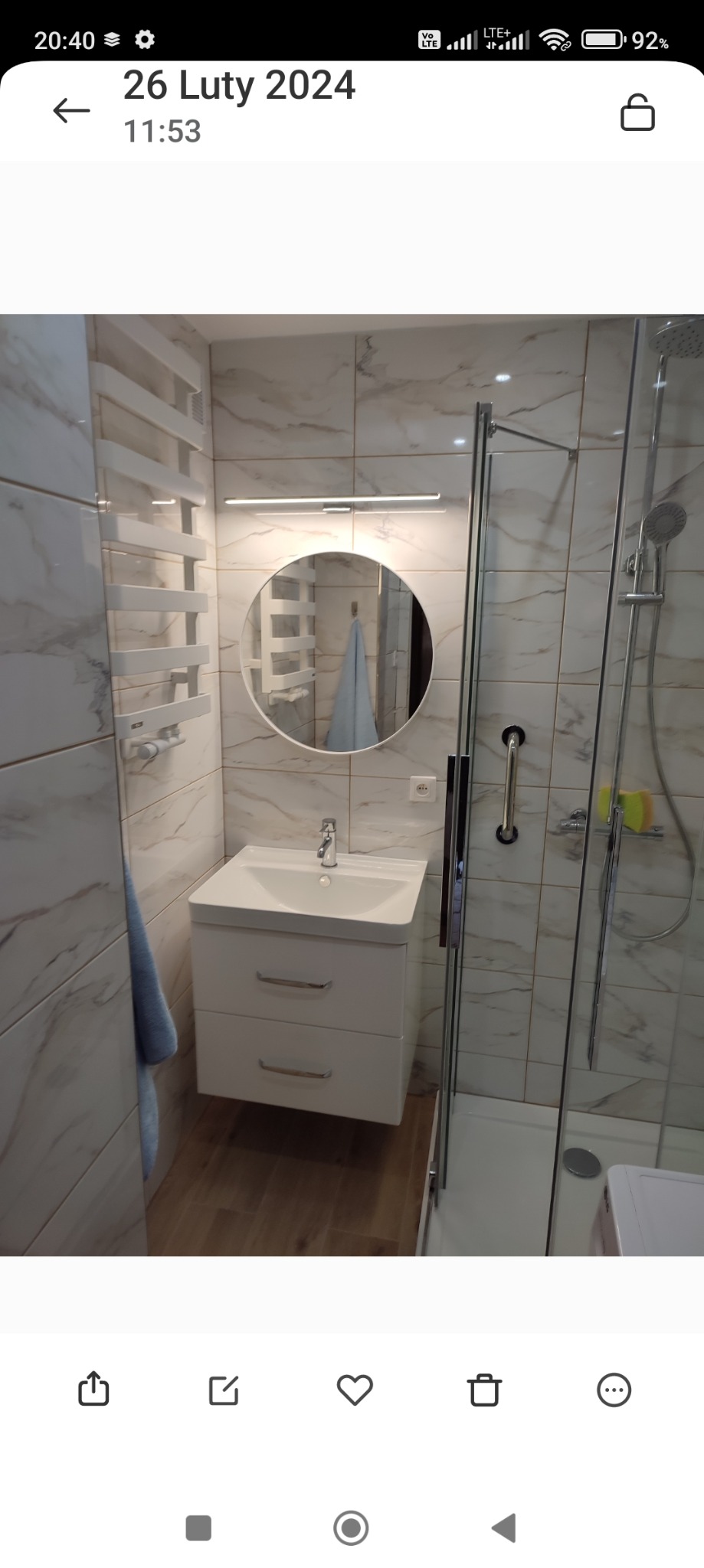 Nowoczesna łazienka z marmurowymi płytkami, kabiną prysznicową ze szklanymi drzwiami, umywalką z szafką, okrągłym lustrem z oświetleniem LED i grzejnikiem drabinkowym.