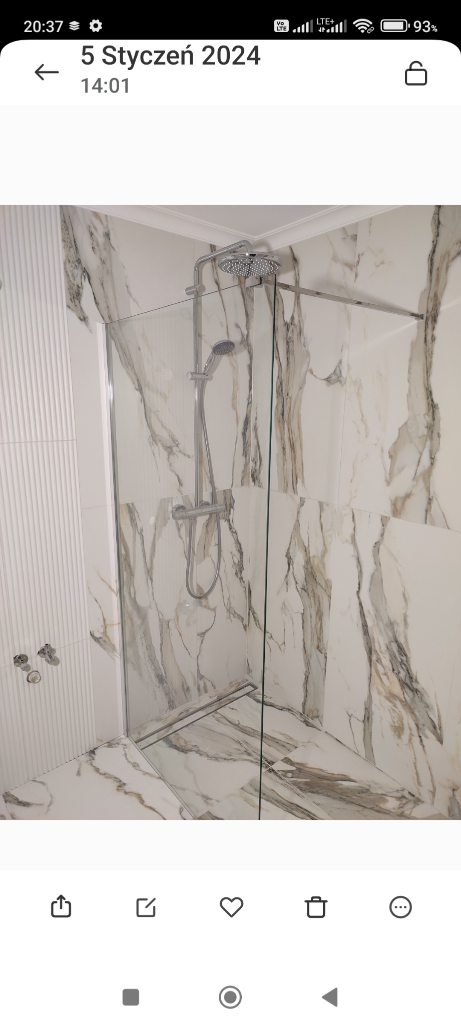 Nowoczesna kabina prysznicowa z chromowaną armaturą i szklaną ścianką, wykończona płytkami imitującymi marmur z delikatnymi żyłami, w minimalistycznej łazience z dekoracyjną ścianą z pionowymi...