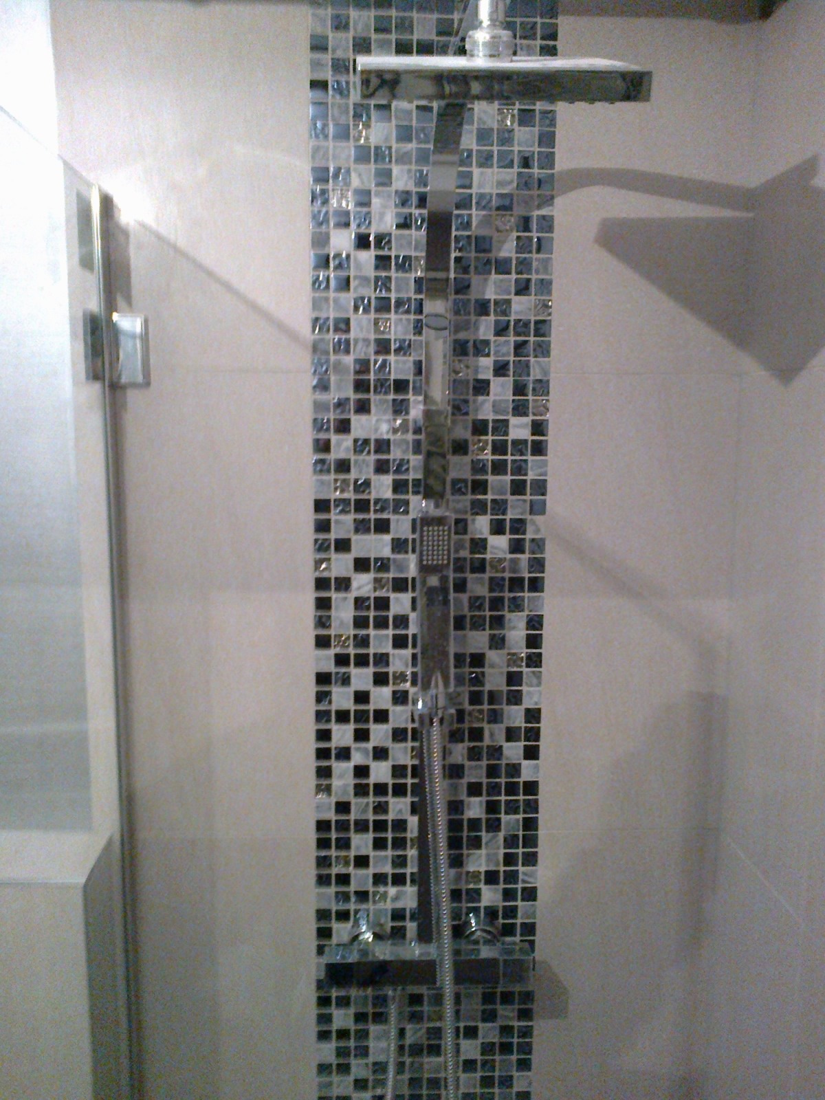 Kabina prysznicowa z deszczownicą i panelem z mozaiki w odcieniach szarości i bieli, widok z boku na szklaną ścianę kabiny.