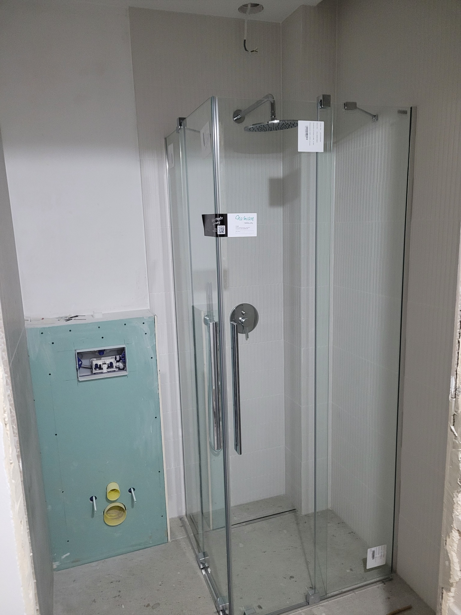Montaż kabiny prysznicowej z deszczownicą w łazience w trakcie wykończenia, widoczna płyta kartonowo-gipsowa z instalacją sanitarną.