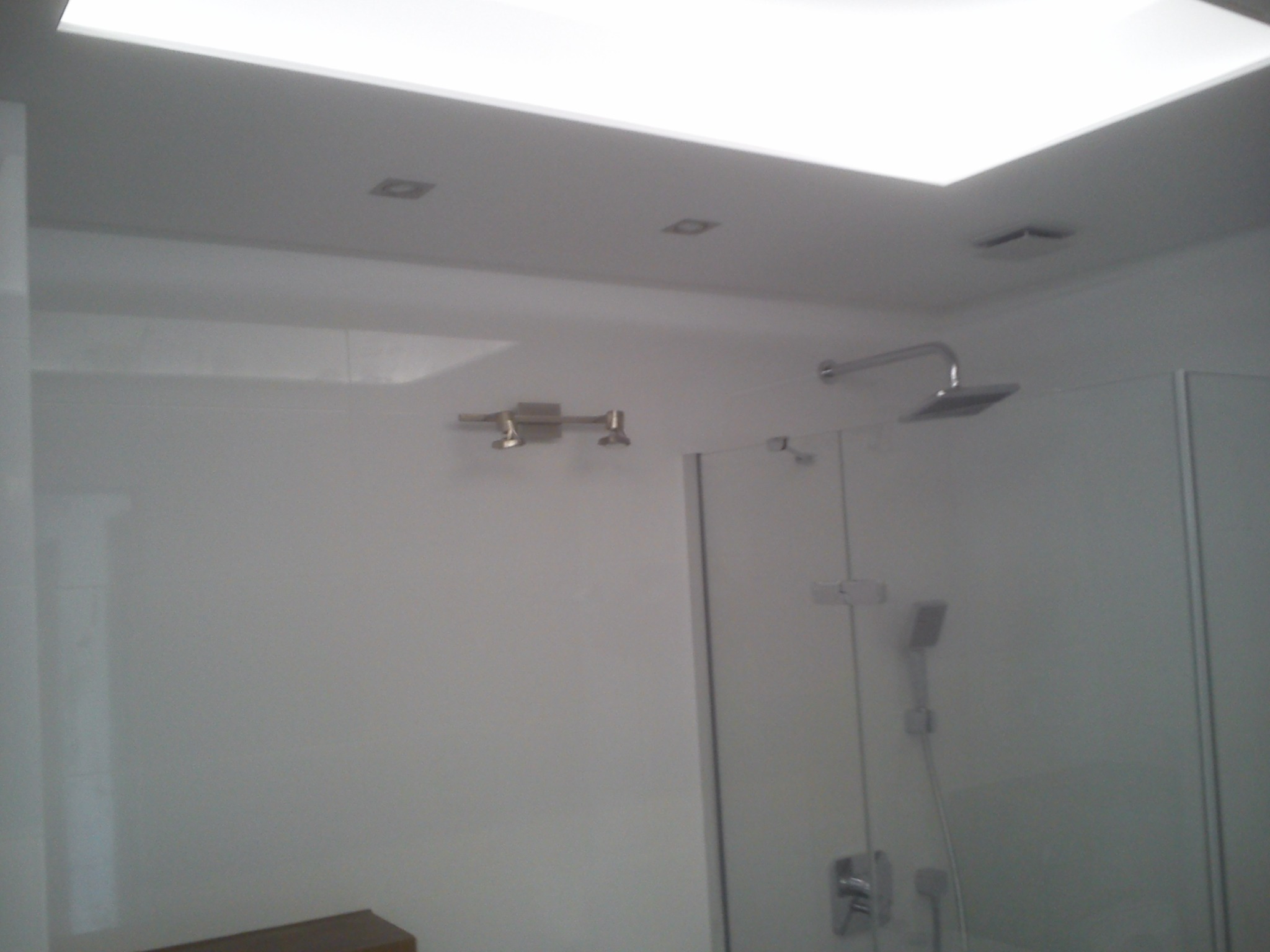 Nowoczesna, minimalistyczna łazienka z przeszkloną kabiną prysznicową, oświetleniem sufitowym i armaturą w kolorze chromu, widziana pod kątem.