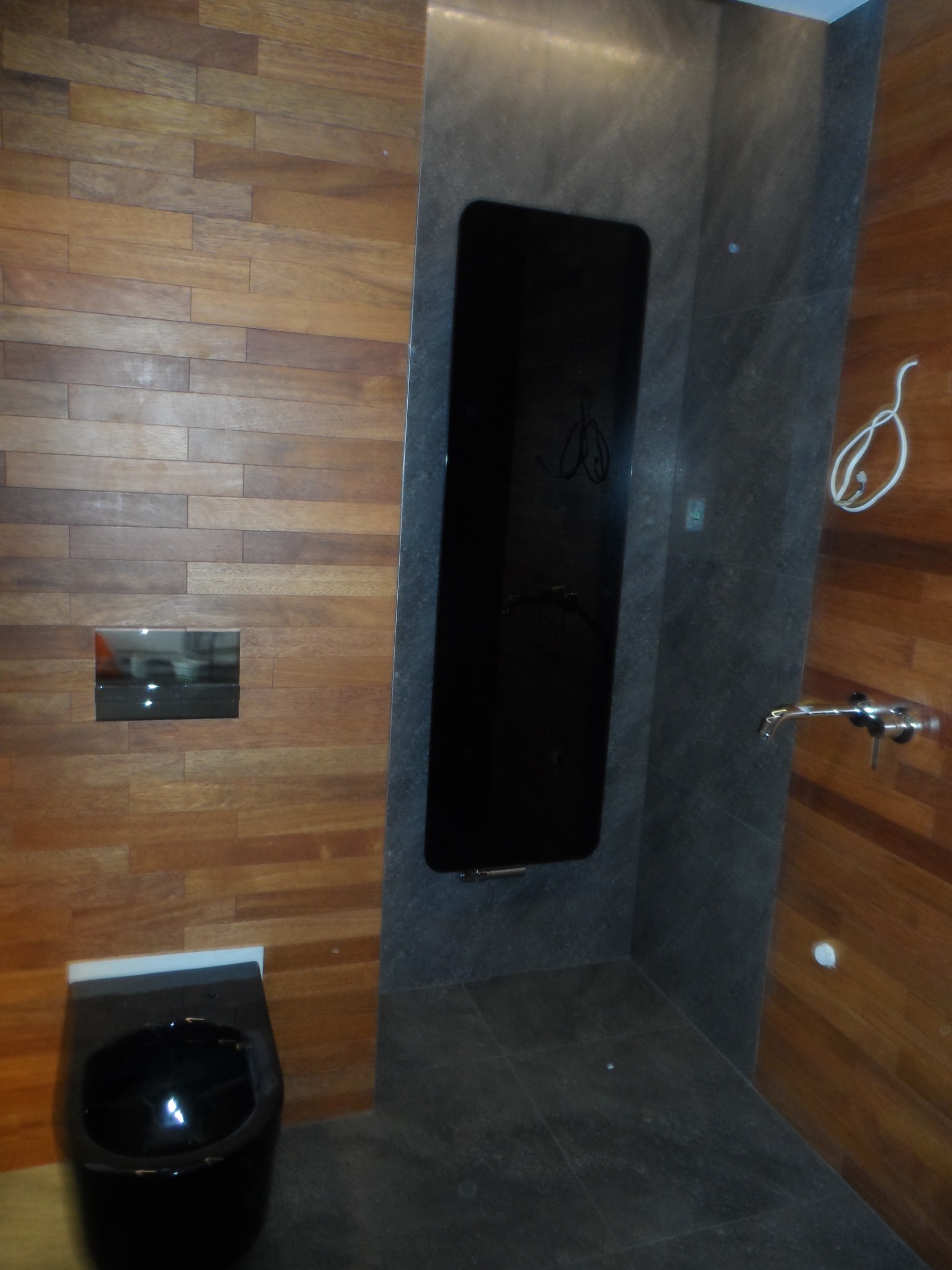 Nowoczesna łazienka we Wrocławiu z drewnianą okładziną ścienną ułożoną w poziome pasy, czarną miską WC, szarą płytką na ścianie i podłodze oraz czarnym, pionowym grzejnikiem.