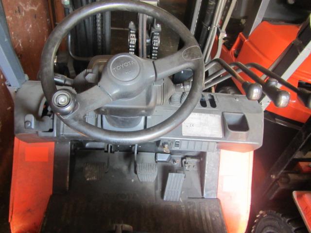 Kokpit wózka widłowego Toyota 7FGF 20 z 2007 roku, widoczne pedały, kierownica z logo Toyota, dźwignie sterujące i fragment pomarańczowej karoserii.