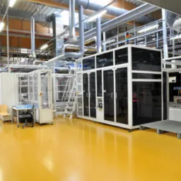 Jasnożółta, bezspoinowa podłoga w hali produkcyjnej z nowoczesnym parkiem maszynowym; widoczne rury wentylacyjne pod sufitem.