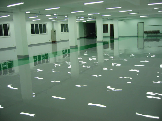 Gładka, szara posadzka przemysłowa z połyskiem odbijająca światła sufitowe w przestronnym, jasnym pomieszczeniu z białymi ścianami i kolumnami.