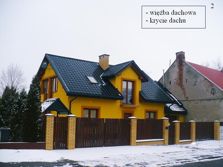 Żółty dom jednorodzinny z ciemną dachówką, widoczny z poziomu ulicy w zimowej scenerii, otoczony drewnianym ogrodzeniem z ceglanymi słupkami. W tle sąsiedni budynek z ceglanym kominem.