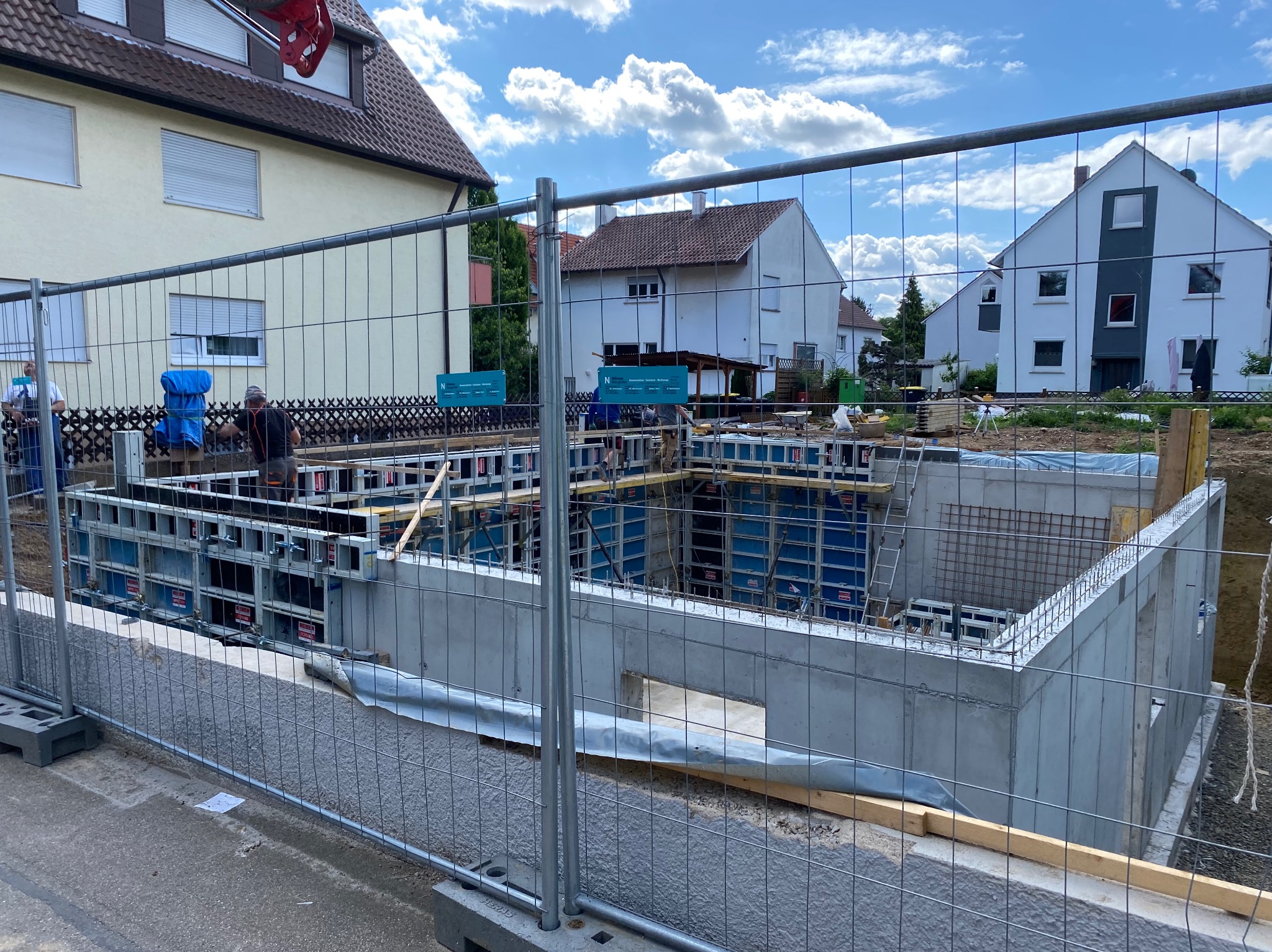 Wykopane fundamenty z betonową wylewką i szalunkiem na budowie domu jednorodzinnego. Widoczne zbrojenia i teren budowy zabezpieczony siatką.