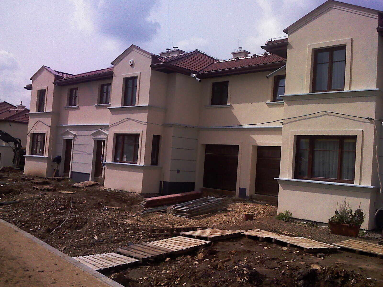 Nowe segmenty domów jednorodzinnych w trakcie wykończenia, widoczne narzędzia i materiały budowlane na niezagospodarowanym jeszcze terenie.