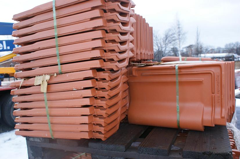 Stosy ceglanych elementów na palecie, zabezpieczone zielonymi taśmami, prawdopodobnie przed montażem na dachu.