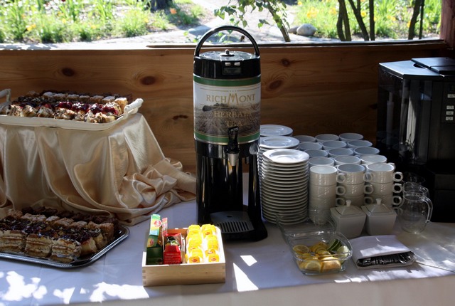 Stół z przekąskami, ciastami, automatem do herbaty Richmont, stosem talerzy i filiżanek, kostkami cukru i cytryną, przygotowany do obsługi gości.