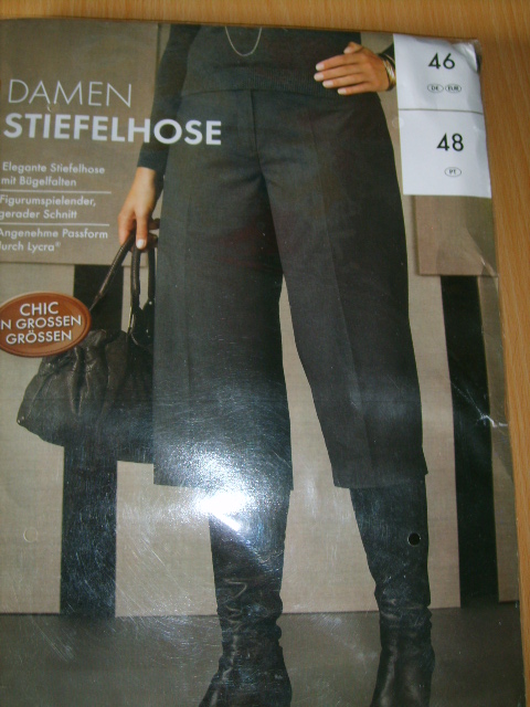 Zdjęcie przedstawia damskie spodnie typu 'stiefelhose' (spodnie do butów) w kolorze grafitowym, z wysokim stanem i szerokimi nogawkami, założone na czarne skórzane kozaki. Na zdjęciu widoczna jest...