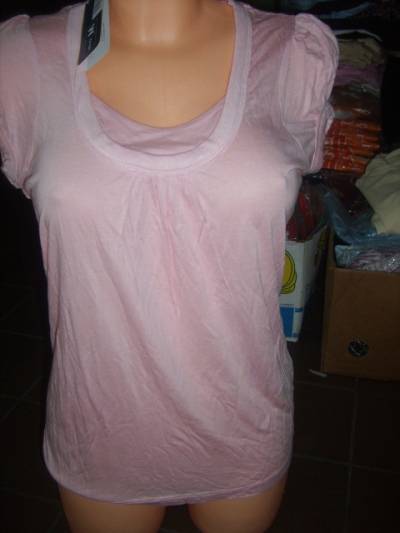 Jasnoróżowa bluzka damska z krótkim rękawem na manekinie, widoczna metka i kartony w tle.