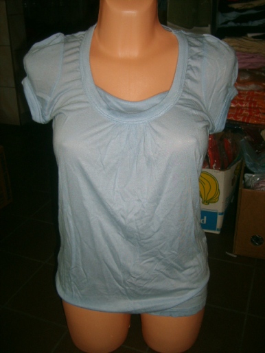 Jasnoniebieska bluzka damska z krótkim rękawem na manekinie, widoczne marszczenia przy dekolcie, tło magazynowe.