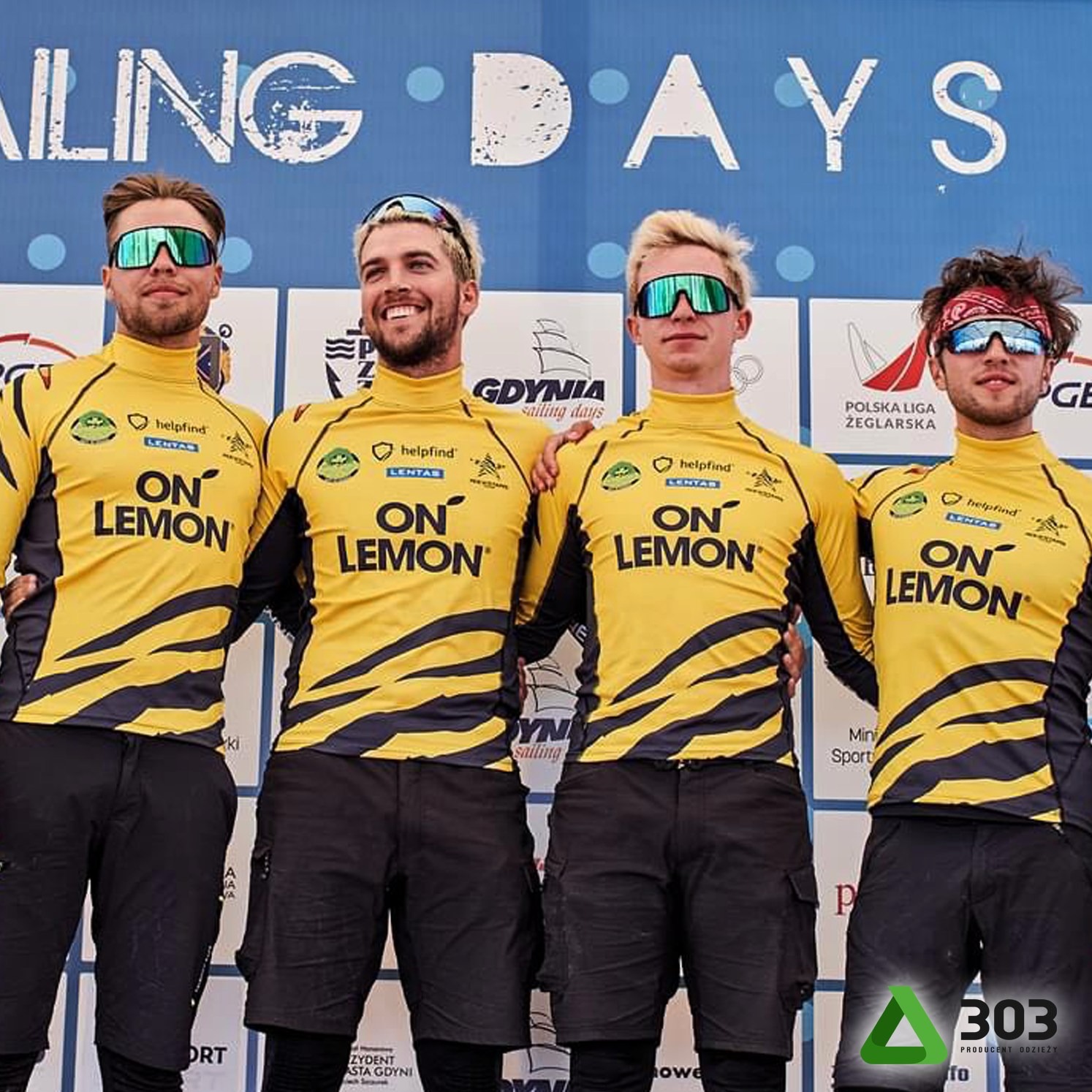 Czterech żeglarzy w żółtych koszulkach z nadrukiem 'ON LEMON' pozuje na tle tablicy 'SAILING DAYS'.