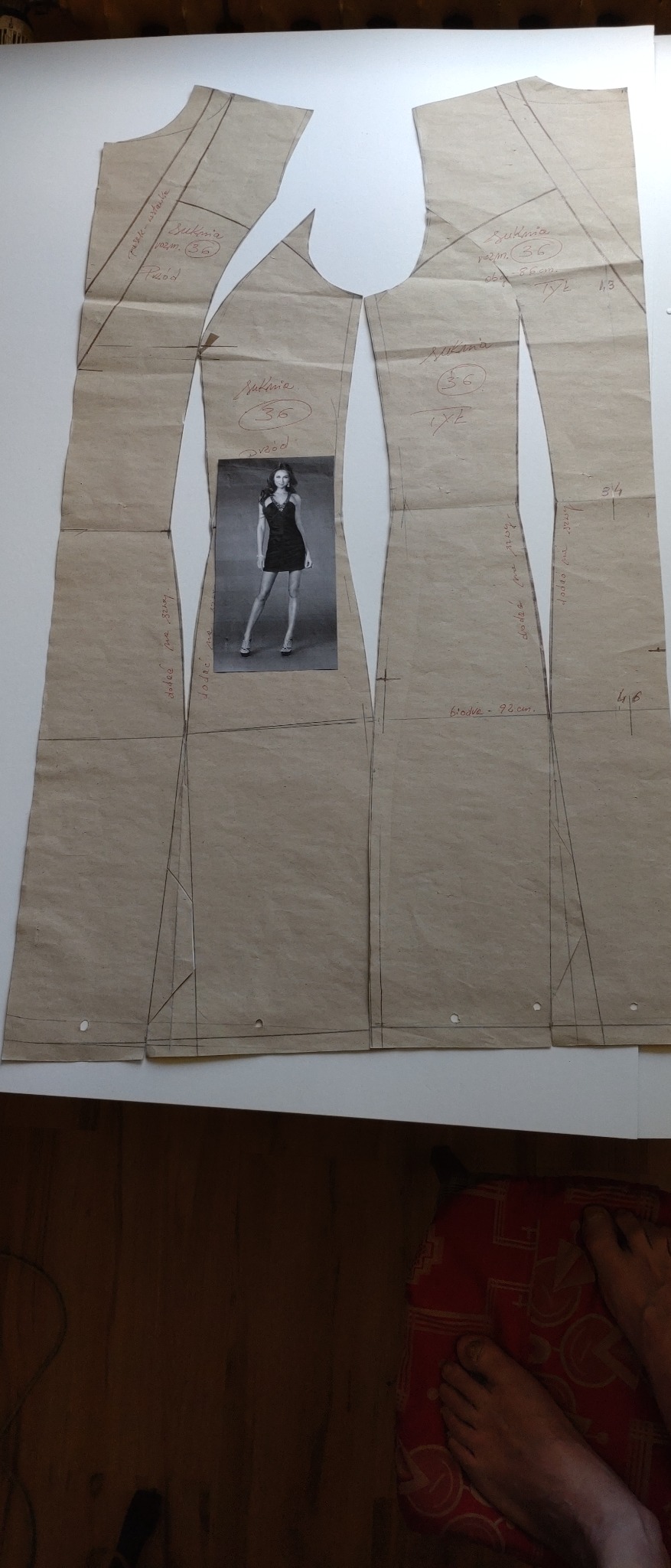 Wykroje sukienki damskiej rozmiar 36 rozłożone na białym stole, obok wklejone zdjęcie modelki w tej sukience, widoczne odręczne notatki i wymiary.