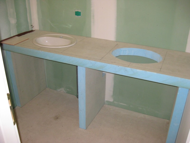 Konstrukcja z wodoodpornych płyt budowlanych przygotowana pod montaż dwóch umywalek w łazience w trakcie remontu, widoczne zaznaczone otwory na umywalki i surowe ściany.