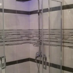 Nowoczesna kabina prysznicowa z chromowaną armaturą i szklanymi drzwiami na tle płytek w odcieniach bieli i szarości z dekoracyjnymi pasami.