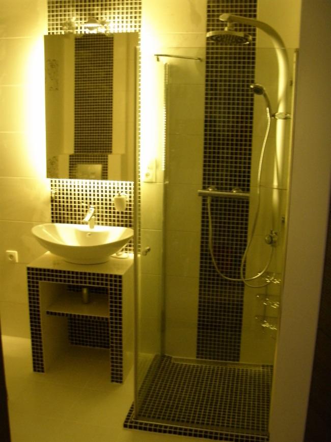 Nowoczesna łazienka z kabiną prysznicową typu walk-in, umywalką nablatową na szafce wykończonej mozaiką i podświetlanym lustrem.