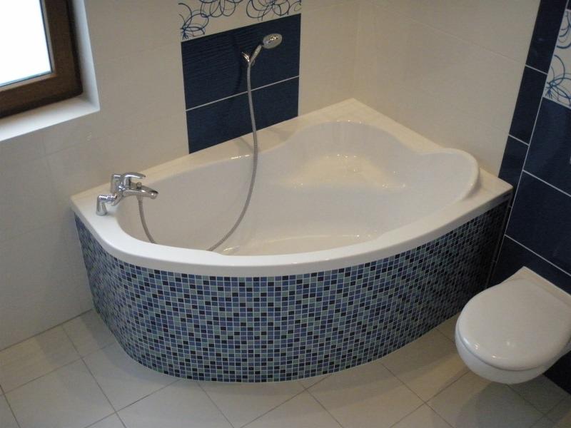 Biała wanna z mozaiką w odcieniach błękitu i granatu, dopasowana do płytek na ścianie. Nowoczesna armatura i kabina prysznicowa. Widoczna toaleta.