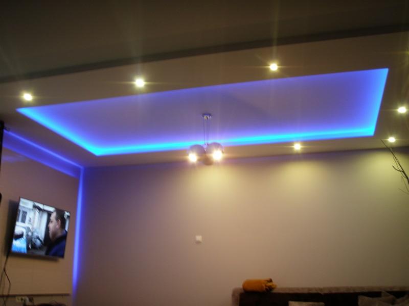 Nowoczesny sufit podwieszany z niebieskim oświetleniem LED, punktowe światła i designerska lampa w salonie z telewizorem. Efektowna aranżacja wnętrza.