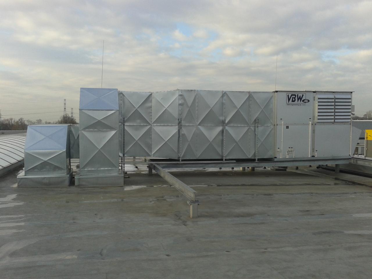 Instalacja wentylacyjna VBW na dachu budynku, widok z boku. Metalowe elementy o kwadratowej strukturze, instalacja na platformie. Pochmurne niebo w tle.
