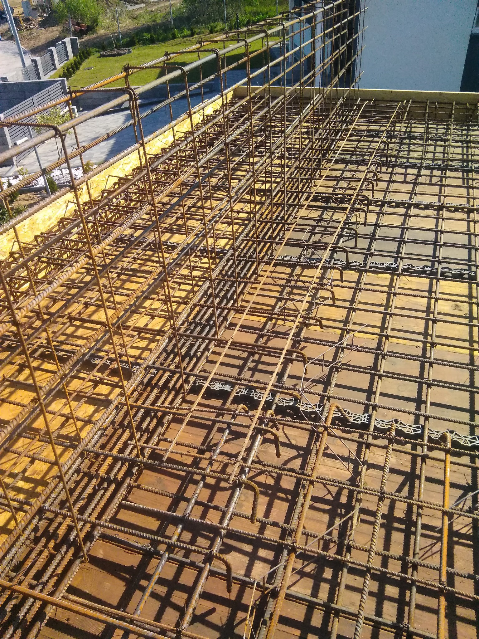 Siatka zbrojeniowa ułożona na żółtej izolacji, przygotowana do zalania betonem, widok z góry na plac budowy.