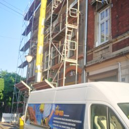 MP-BUD Usługi Budowlane - Budynek w trakcie renowacji elewacji z rusztowaniem i żółtym zsypem na gruz, na pierwszym planie samochód firmy budowlanej z reklamą usług dekarsko-blacharskich i dociepleń.